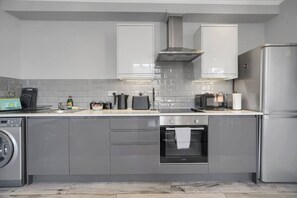 A modern kitchen with grey cabinets, a stainless steel range hood, a built-in oven, a microwave, and a refrigerator. - Spacious | Cardiff Central | Fast Wifi | Netflix (Cardiff)
