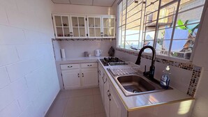 A compact kitchen with white cabinets, a sink, and a window with a view of the outside. - Your Home way From Home (San Salvador)