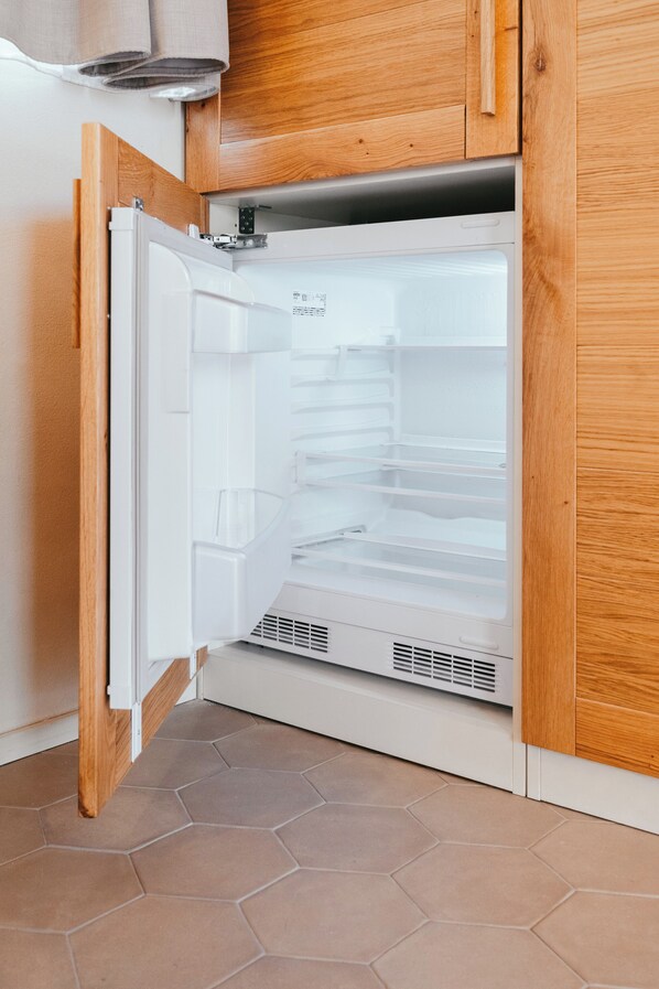 A kitchen with a white refrigerator, wooden cabinets, and a hexagonal tile floor.