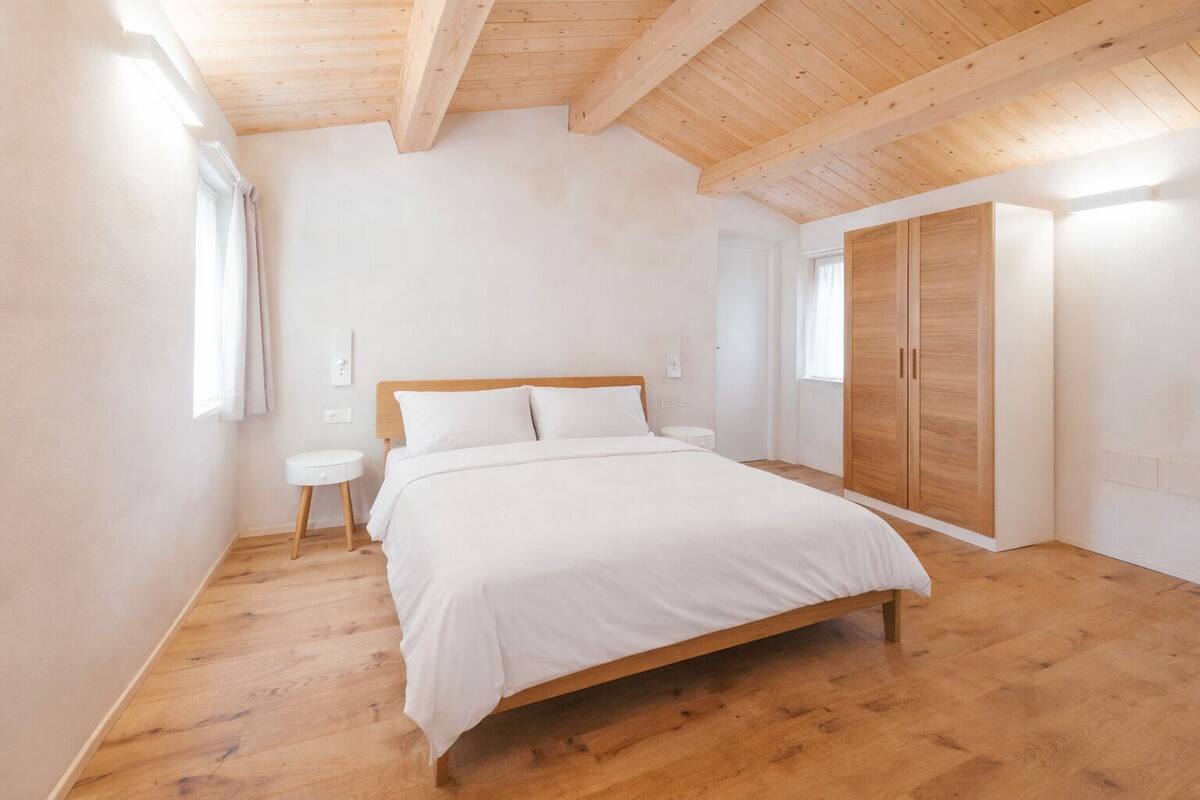 Un dormitorio con techo de madera, una cama, un armario y una mesita de noche.