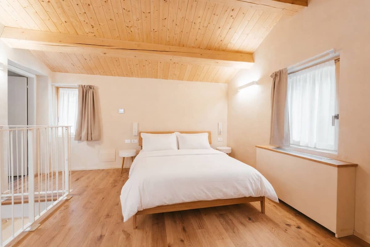 Un dormitorio con una cama de madera, una ventana con cortinas, una mesita de noche y suelo de madera.