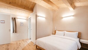 Une chambre avec un plafond en bois, un lit avec une literie blanche, une table de chevet et une porte donnant sur une autre pièce.