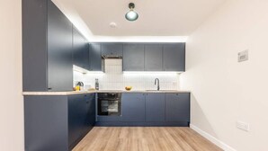 A compact kitchen with dark cabinets, a wooden countertop, a built-in oven, and a single light fixture. - Luxurious 2 Bed | Central Cardiff | Free EV Charge (Whitchurch)