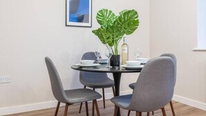 A dining area with a round table, four grey chairs, a potted plant, and a wine bottle. - Luxurious 2 Bed | Central Cardiff | Free EV Charge (Whitchurch)