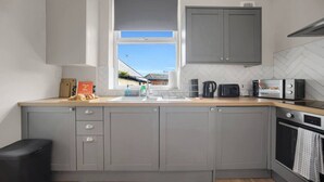 Una cucina moderna con mobili grigi, un piano di lavoro in legno, una finestra e vista su un edificio.