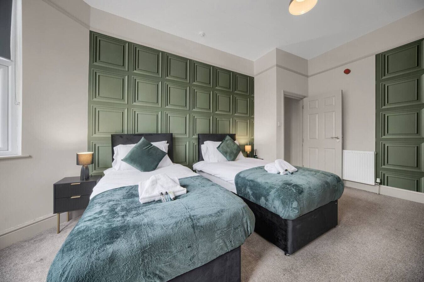 Een tweepersoonskamer met twee bedden, een nachtkastje, een lamp en een radiator.