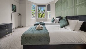Camera da letto con due letti, una cassettiera, una lampada da terra e una finestra vista alberi.