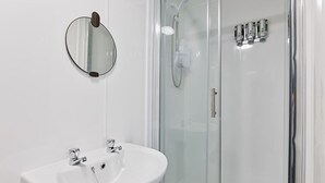A bathroom with a white sink, a round mirror, and a glass-enclosed shower. - Private En-Suite • TV • Fridge • Microwave (Saint Thomas)