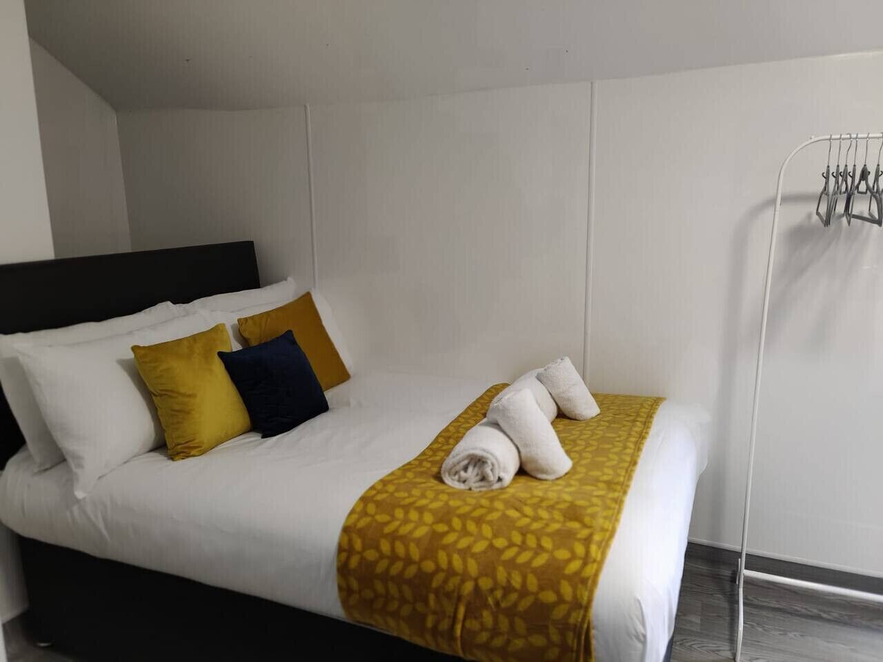 A neatly made bed with a patterned blanket, two pillows, and rolled towels.