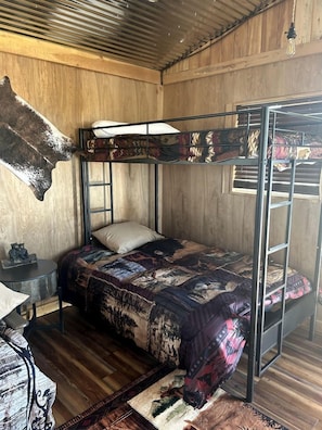 A bunk bed with a patterned bedspread, a small table with a bear figurine, and a wooden floor.