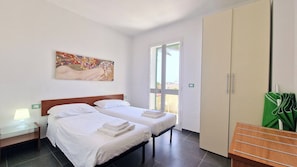 A hotel room with two beds, a large window, a wardrobe, and a painting on the wall.