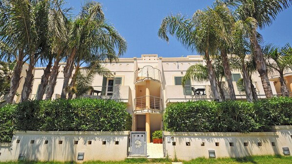 A building with a central entrance, balconies, and surrounding palm trees.