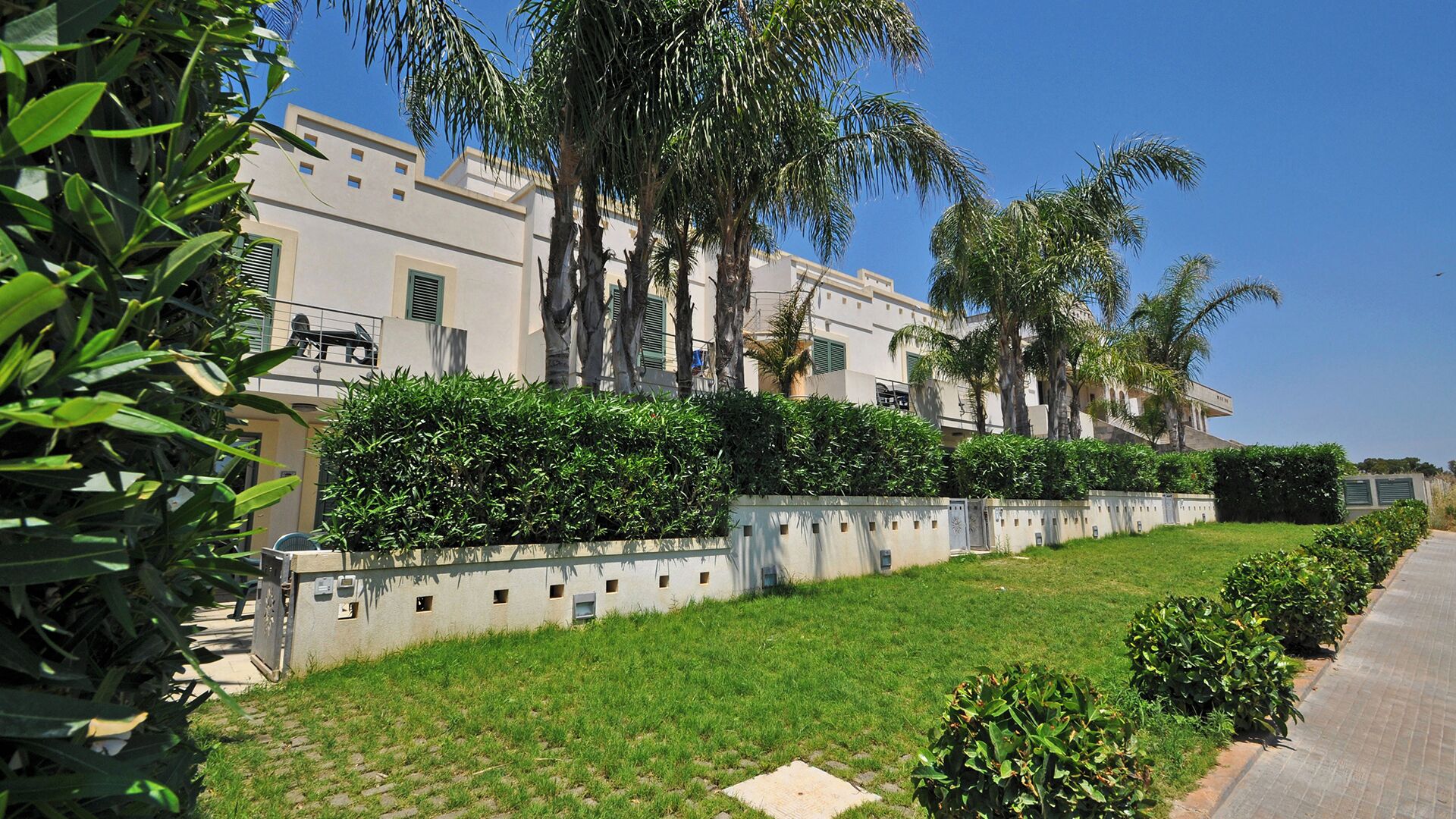 A residential building with a well-maintained lawn, palm trees, and a clear sky.