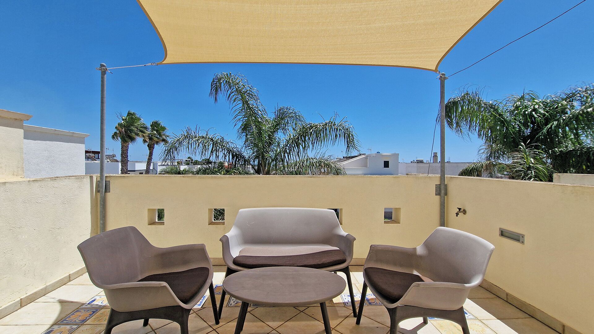 A patio with a table and chairs, a beige canopy, and a view of palm trees and buildings.
