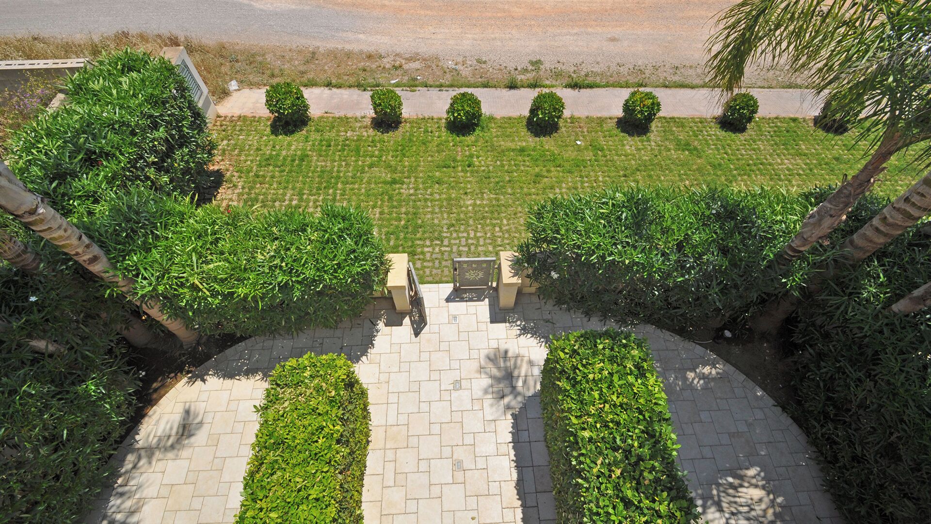 A paved pathway leading to a seating area with a view of a well-maintained lawn and a road in the background.