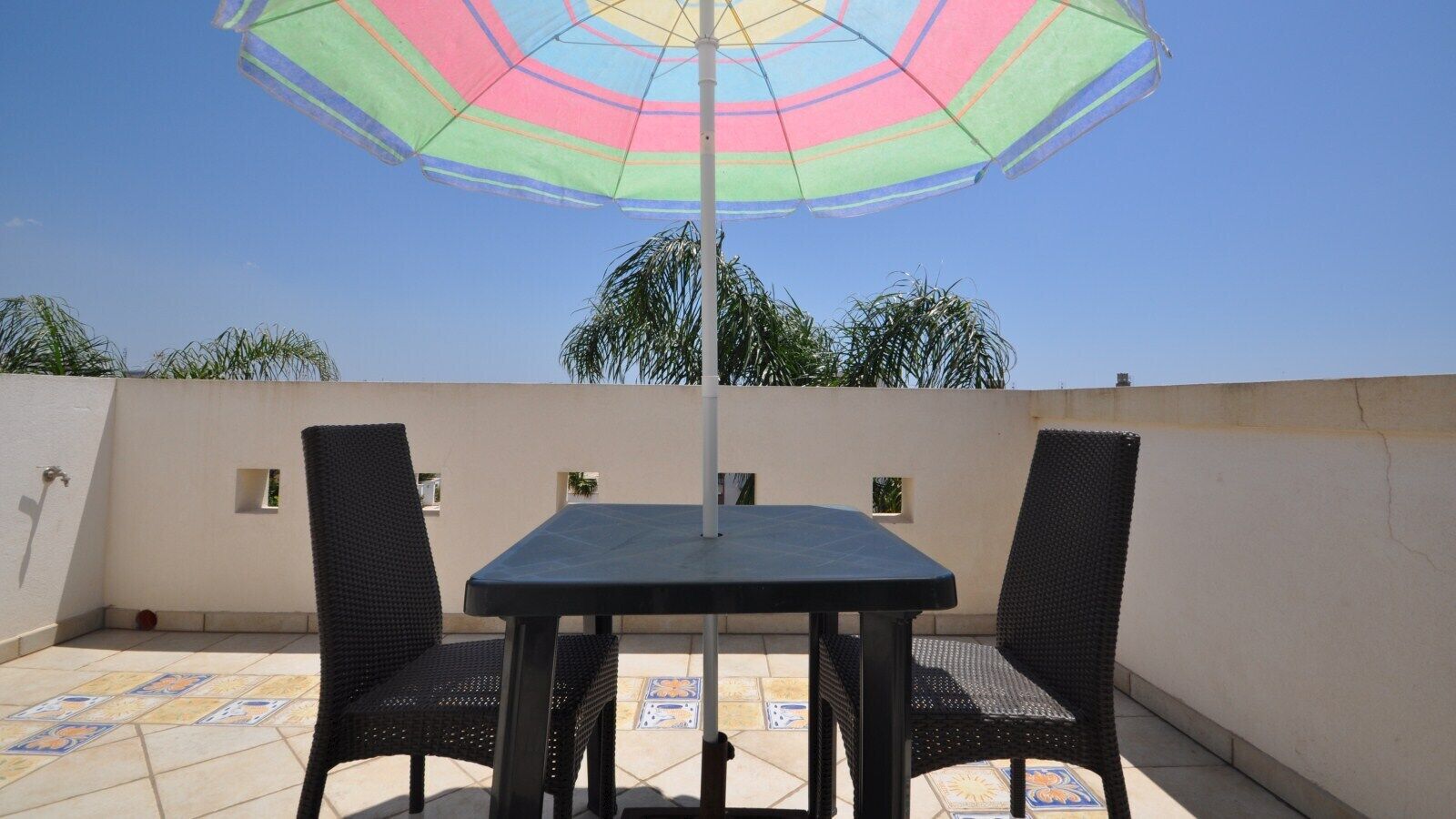 Une terrasse extérieure avec une table et deux chaises, un parasol et un sol carrelé.