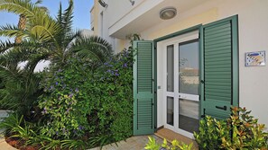 A building with a green door, a small porch, and a garden with various plants and flowers.
