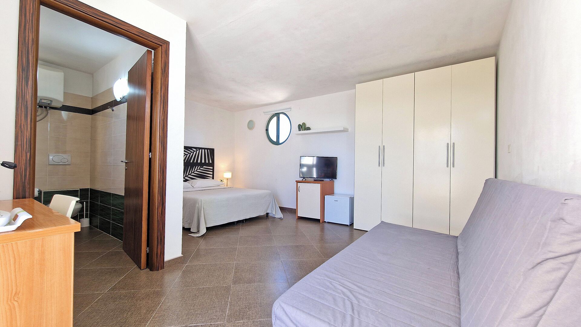 A hotel room with a bed, a desk, a television, a wardrobe, and a bathroom.