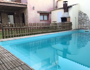 Une piscine avec une terrasse en bois, un mur en pierre et une cheminée en métal.