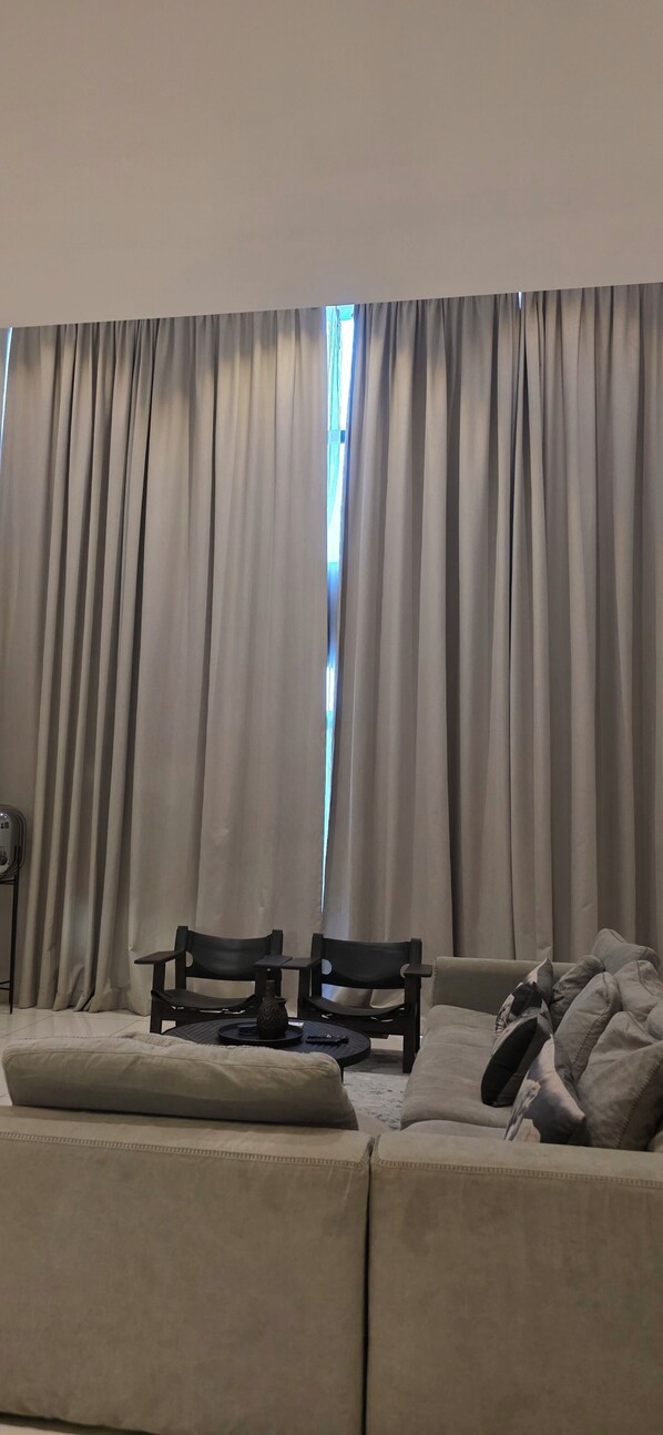 A living room with a sofa, two chairs, a table, and a window with curtains. - EBS Properties At Embassy Garden (Accra)
