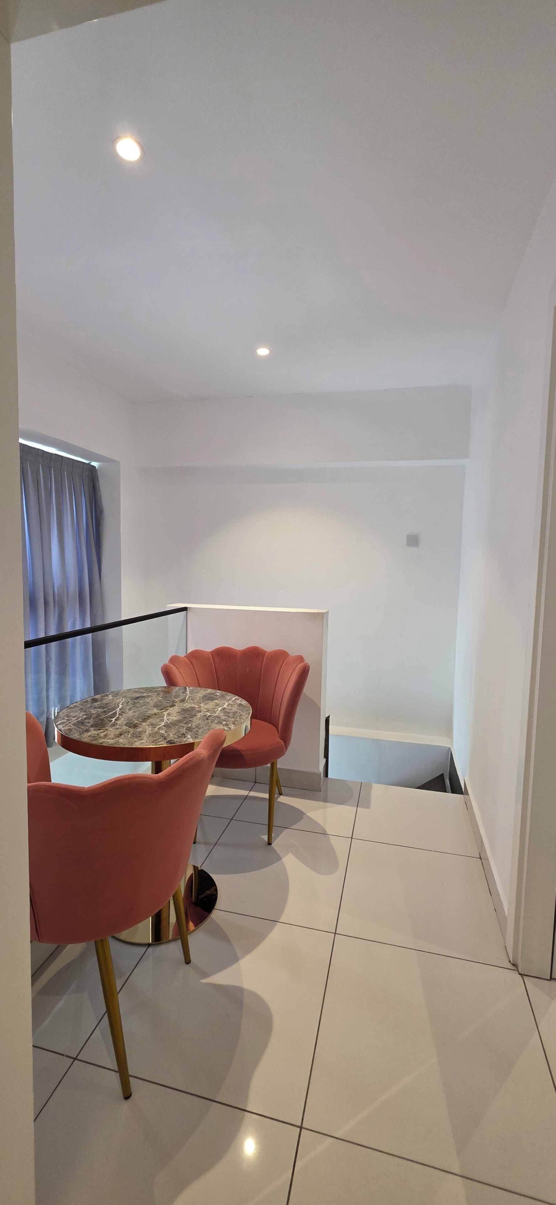 Un intérieur moderne avec une table ronde et deux chaises, un balcon doté d’une balustrade et une vue sur l’extérieur.