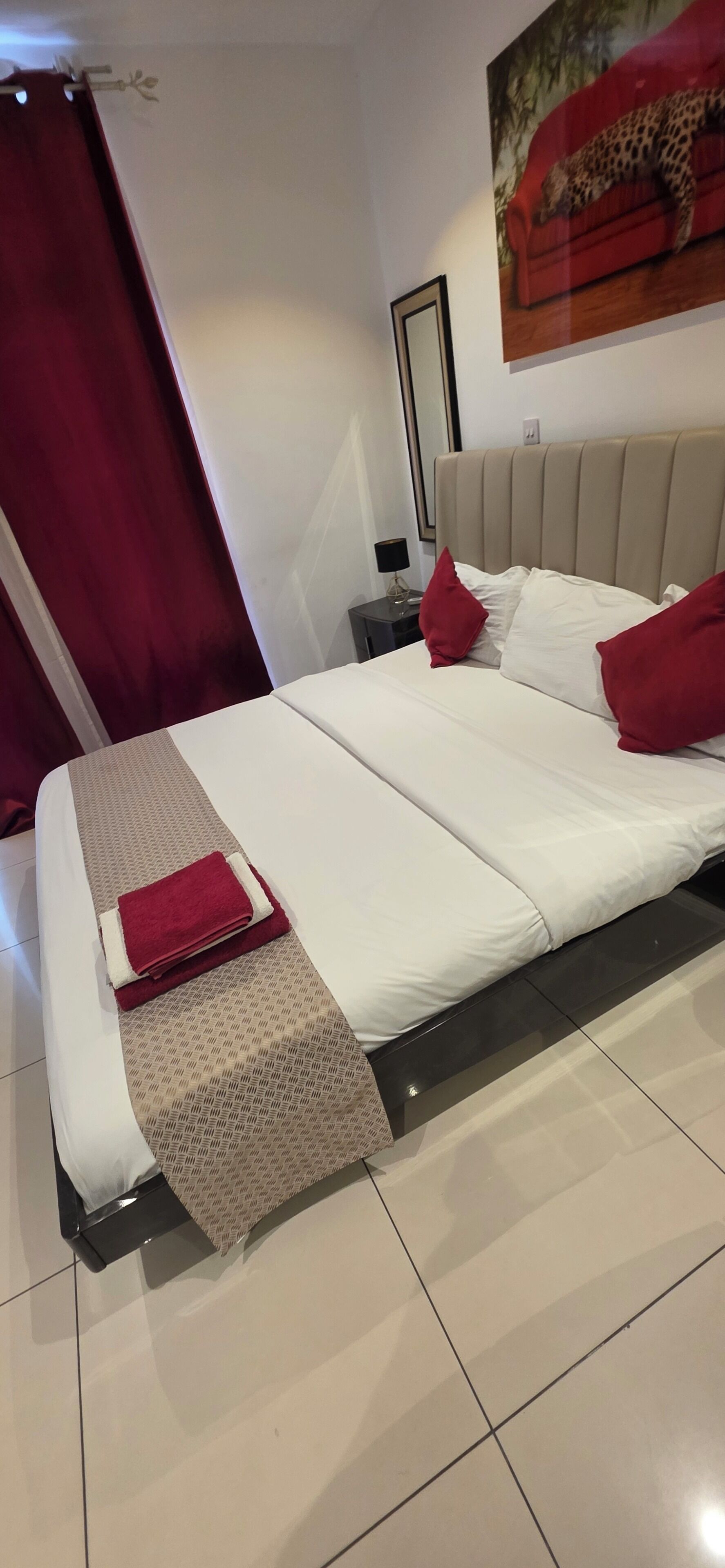 Een netjes opgemaakt bed met een bedsprei met patroon, een rode plaid en passende kussens.