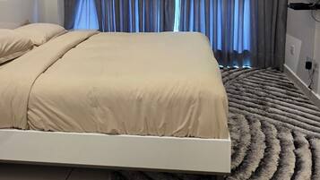 Een moderne slaapkamer met een bed, gordijnen, een televisie en een kamerkleed met een patroon.