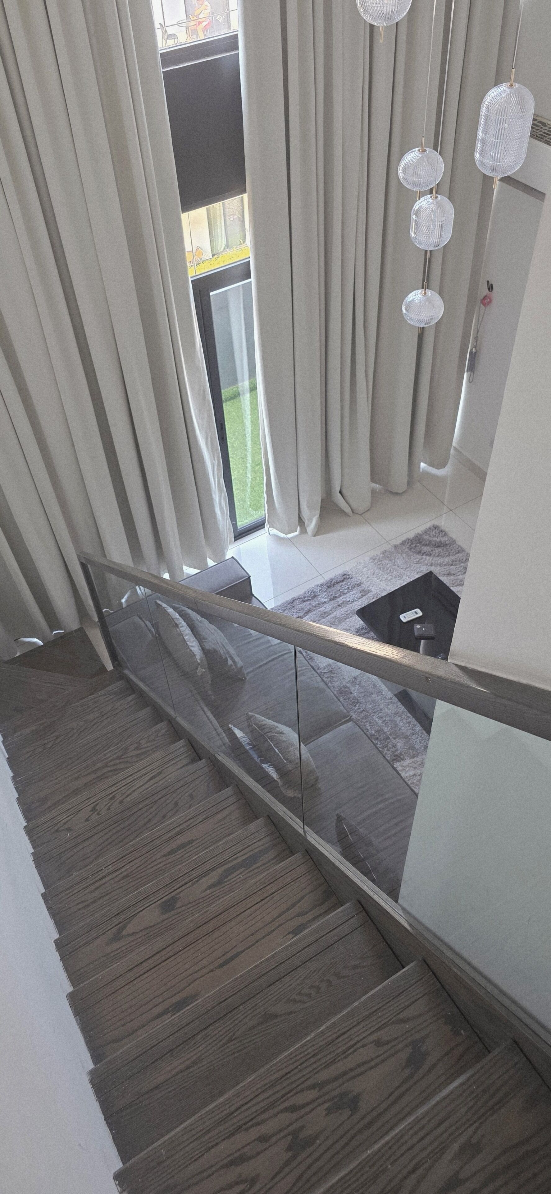 A staircase with wooden steps, a glass railing, and a view of a balcony with curtains.