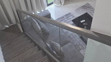 A staircase with wooden steps, a glass railing, and a view of a balcony with curtains.