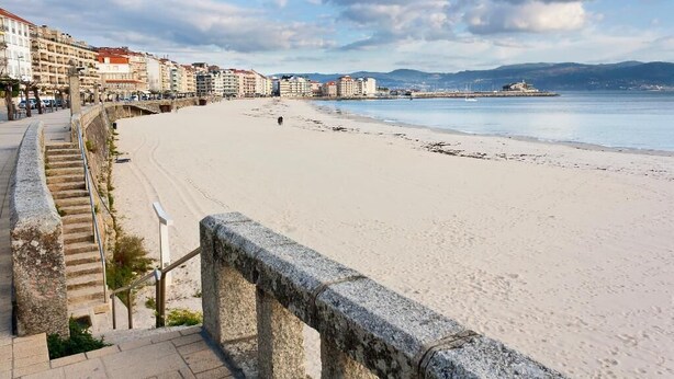 A coastal promenade with a stone staircase leading to a beach, buildings in the background, and a clear sky. - Stylish Beachside Apartment | Ocean Views, 380m from Playa de Silgar, Sanxenxo (Sanxenxo)