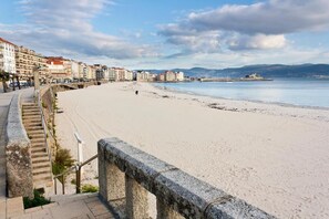 Eine Küstenpromenade mit einer Steintreppe, die zu einem Strand führt, mit Gebäuden im Hintergrund und wolkenlosem Himmel.