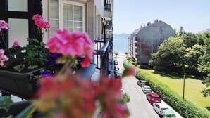 A balcony with potted flowers, a view of a road, and a building with a balcony. - Stylish Beachside Apartment | Ocean Views, 380m from Playa de Silgar, Sanxenxo (Sanxenxo)