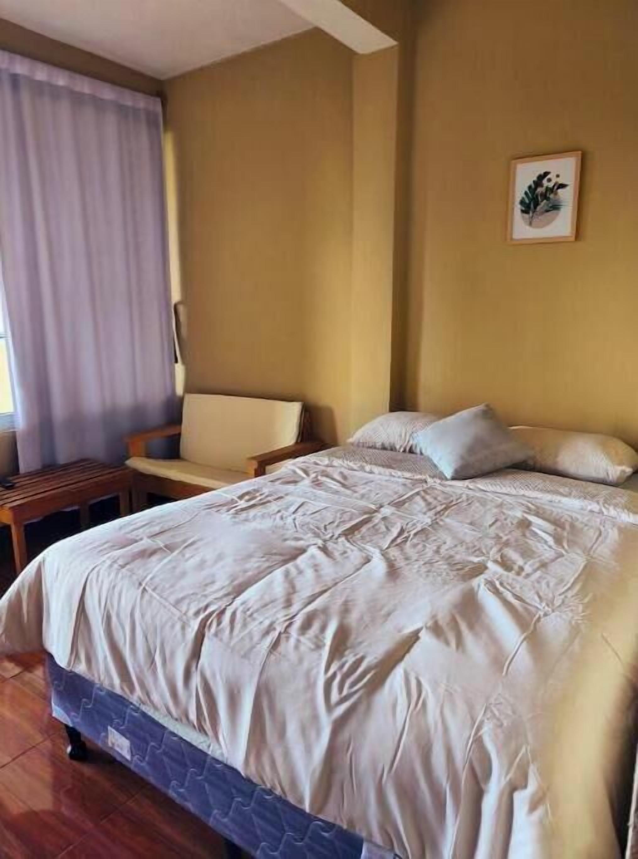 A bedroom with a bed, a chair, a small table, and a wall-mounted picture.