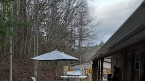 A wooden deck with picnic tables and a grill, surrounded by trees. - Creekside Garage Getaway  (Robbinsville)