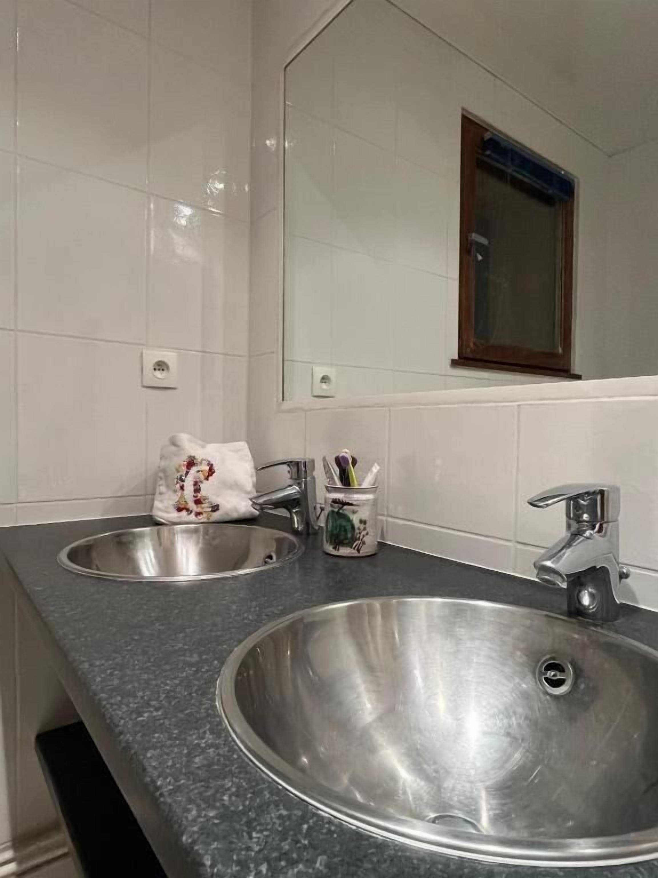 A bathroom with two stainless steel sinks, a mirror, and a window.