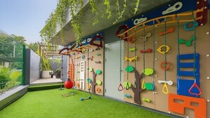 Zona de juegos infantiles con paredes de escalar, canasta de baloncesto y césped artificial.