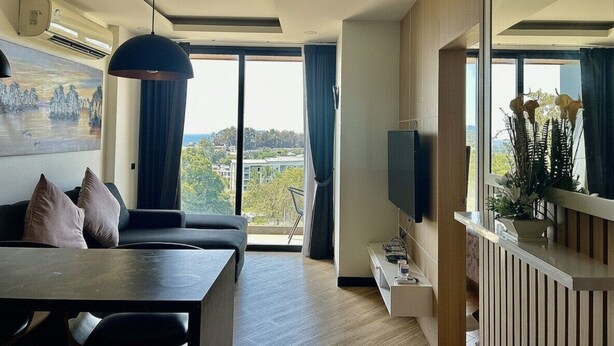 Una sala moderna con sofá, mesa de comedor, televisor y un ventanal con vistas a la ciudad.