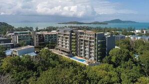 Un hotel de varios pisos con piscina, rodeado de vegetación y vistas al mar.