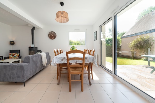 A modern living room with a dining table, chairs, a sofa, a fireplace, and a large window.