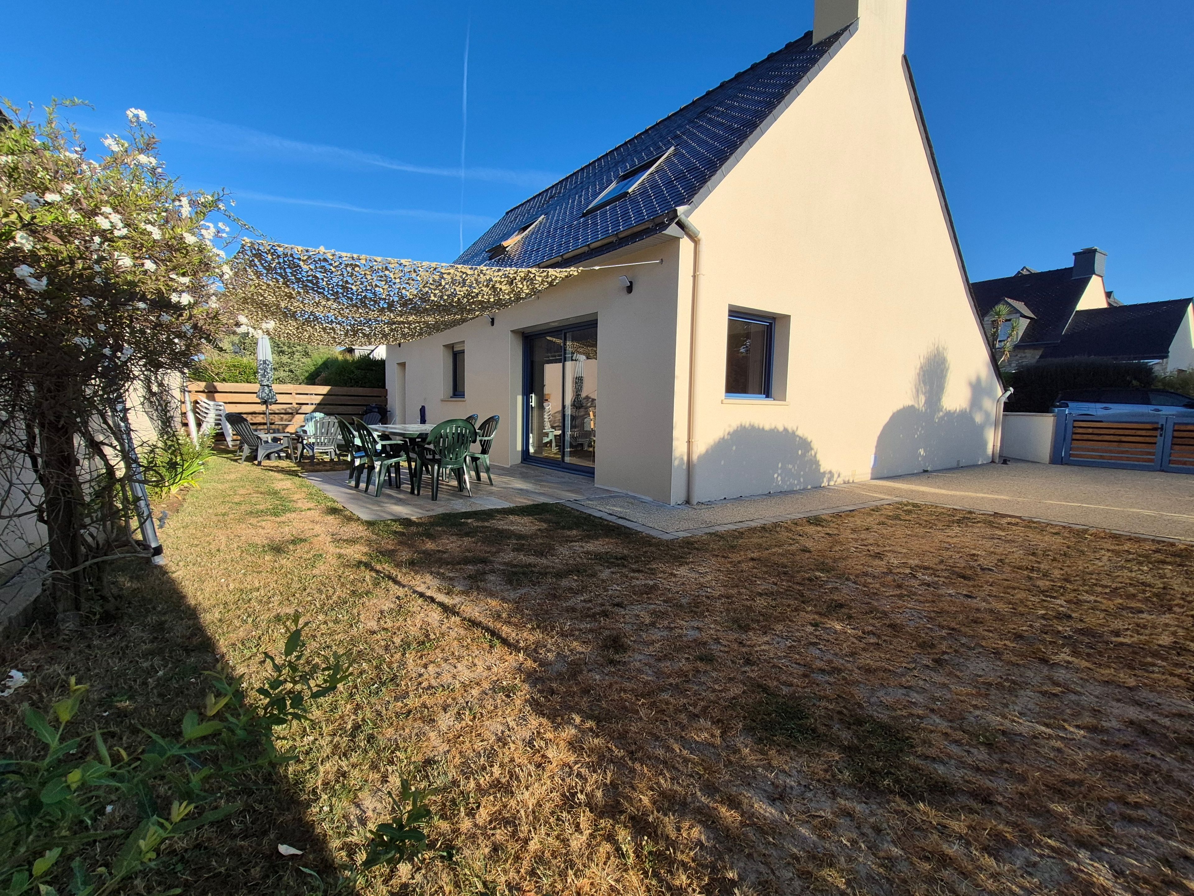Ett modernt hus med ett sluttande tak, en uteplats med utemöbler och en klarblå himmel.