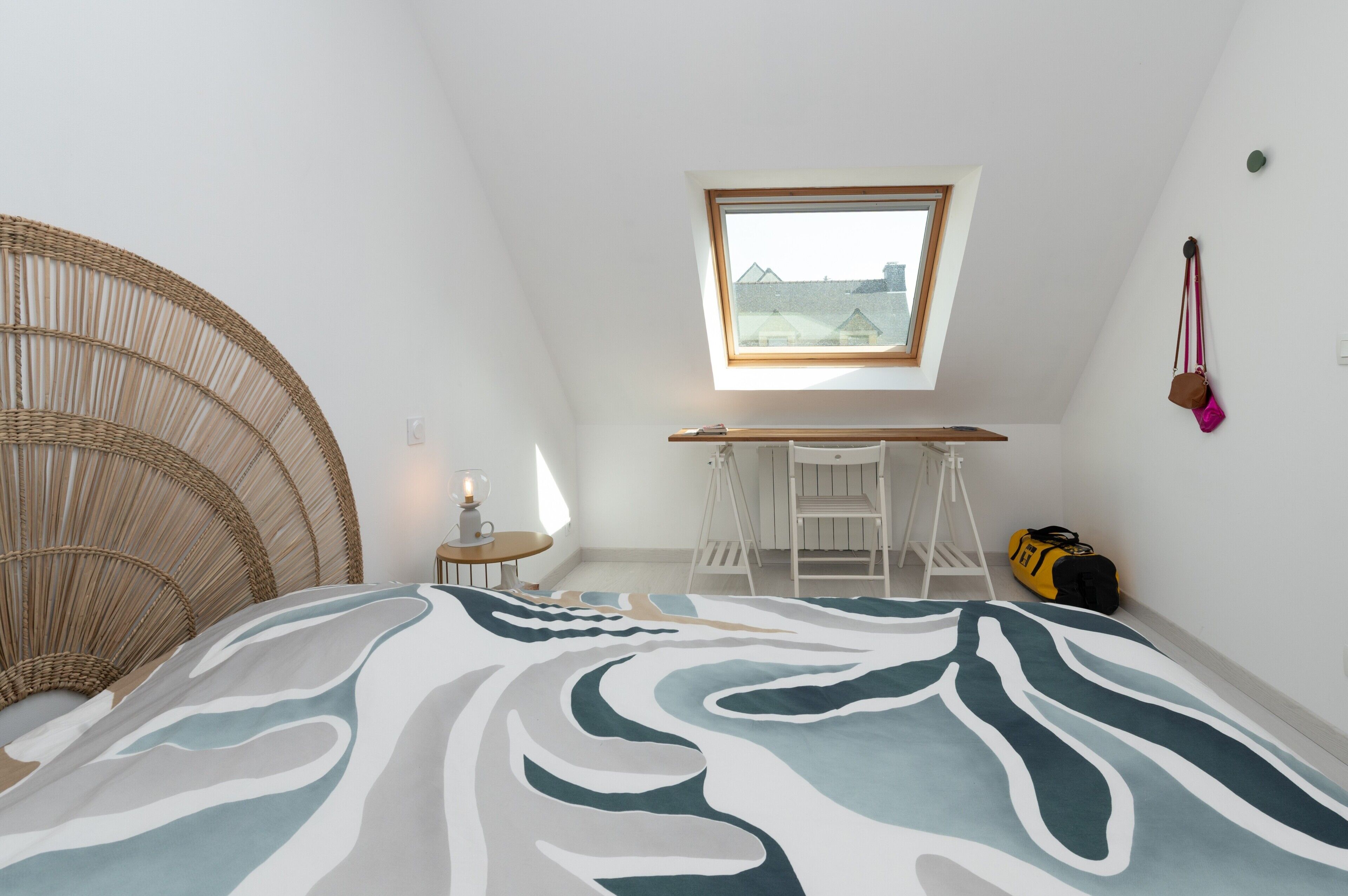 A bedroom with a bed, a desk, a chair, a window, and a hanging bag.