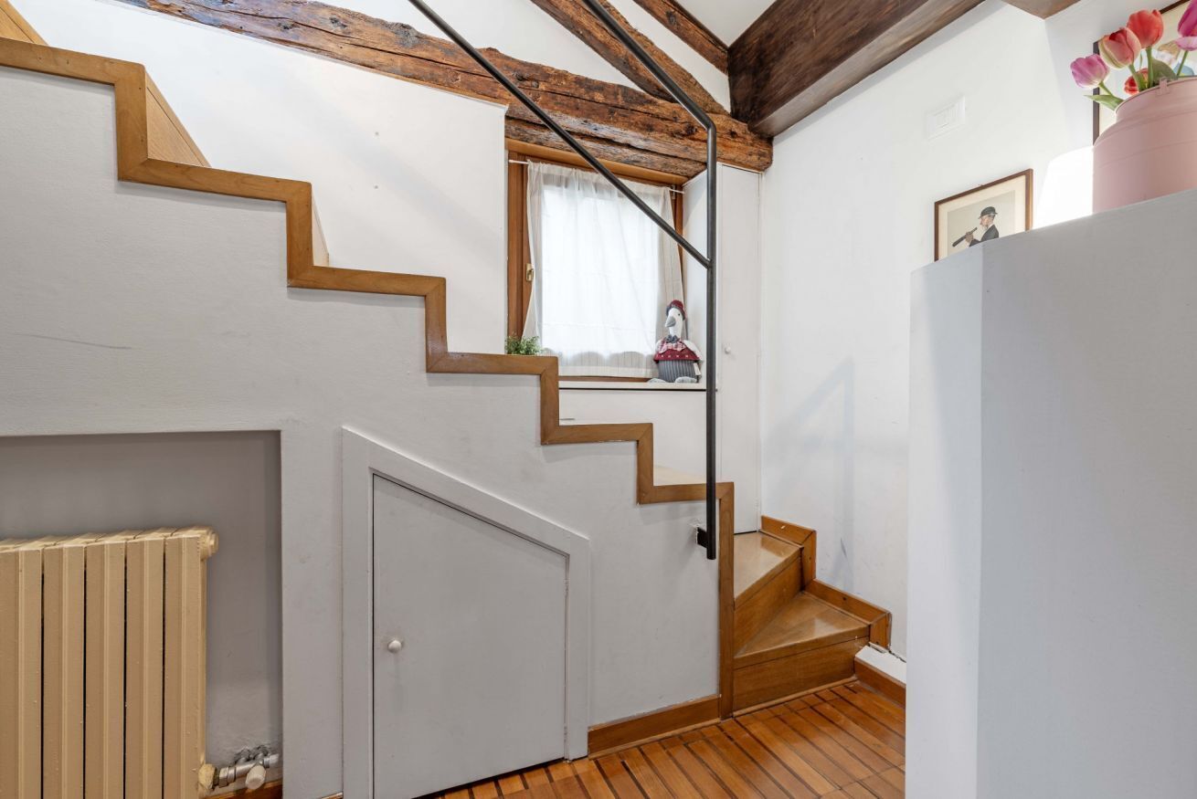 A staircase with wooden steps and a white door, a radiator, and a window with a curtain.