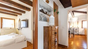Un dormitorio con cama, suelo de madera, tocador, un cuadro y un rincón comedor con sillas y mesa.