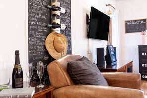 A cozy living room with a leather sofa, a television, a chalkboard with names and messages, wine bottles, glasses, and a straw hat. - Modern apartment in the heart of San Marco - 2 bedrooms (Venice)