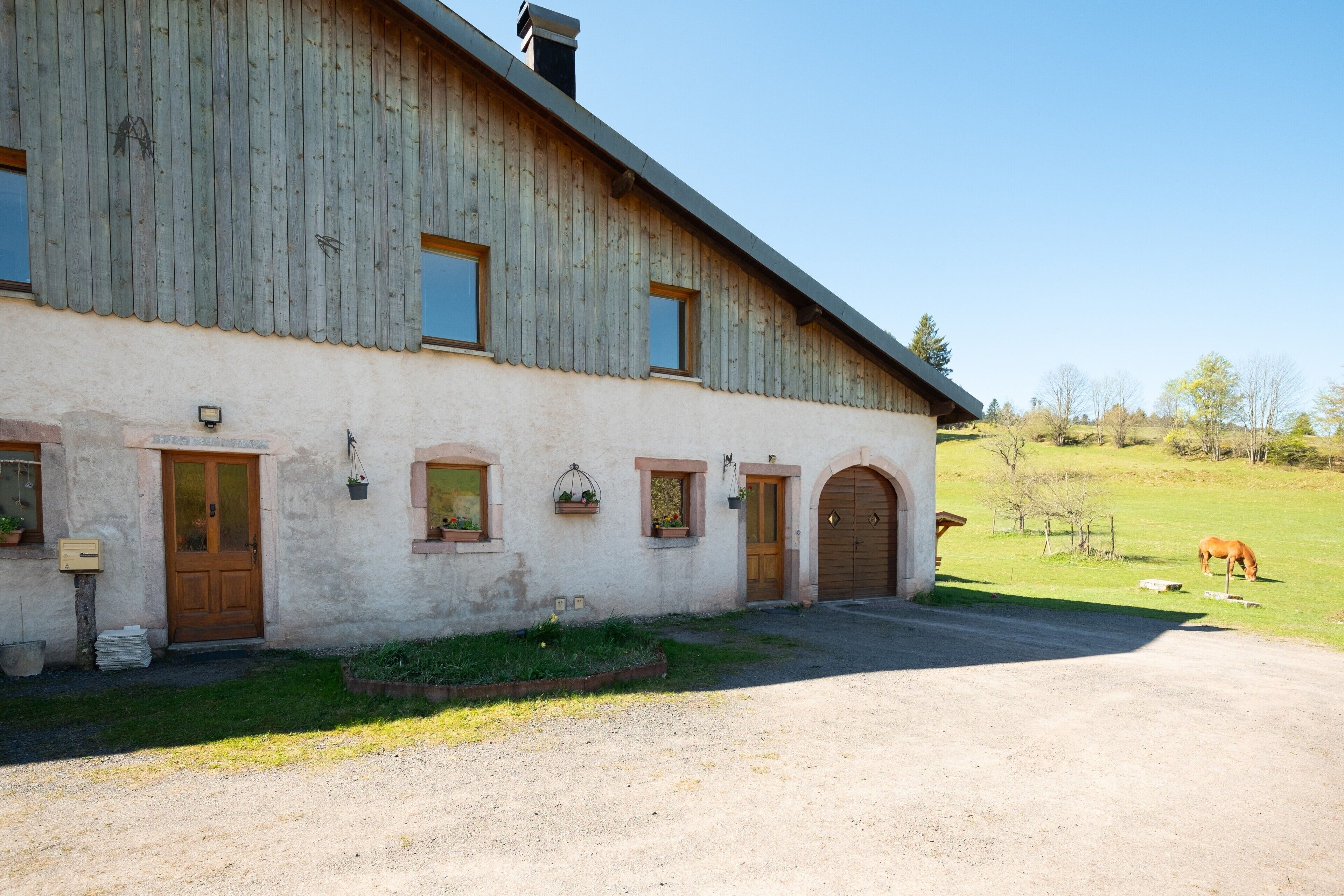 Une grange rustique avec une allée en terre battue, des portes en bois et des fenêtres en arc de cercle.