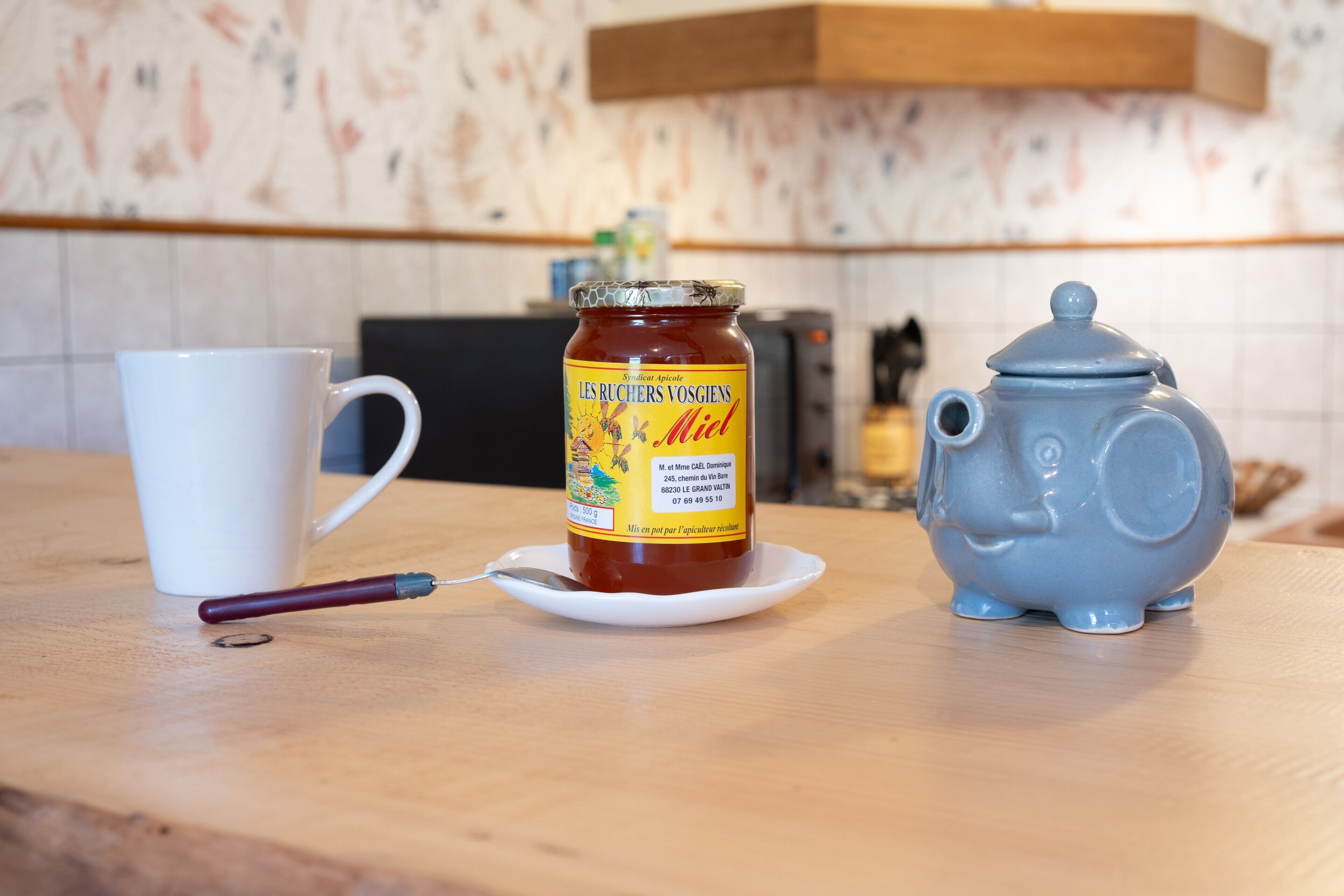 Una encimera de cocina con un tarro de miel, una tetera y una taza blanca.