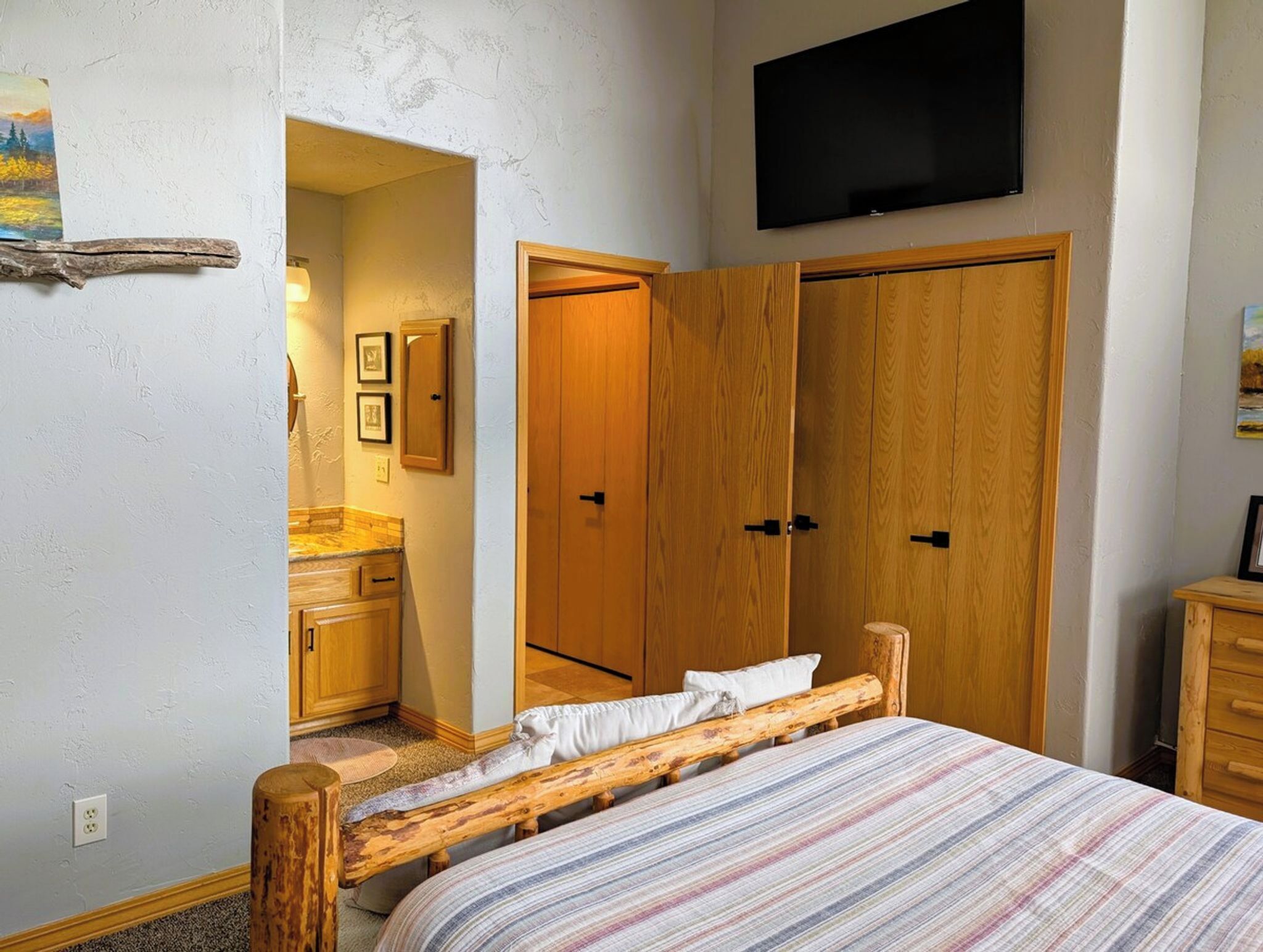 A bedroom with a bed, wooden wardrobe, a television, and a small bathroom.