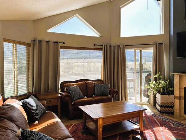A spacious living room with a sofa, a wooden coffee table, and a large window with curtains.
