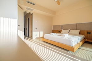 A modern hotel room with a large bed, a wooden headboard, and a view of the hallway.