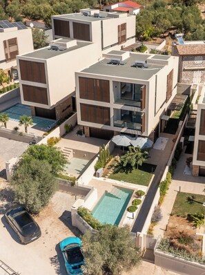 A modern multi-story building with a rooftop pool, outdoor seating, and a car parked in the driveway.